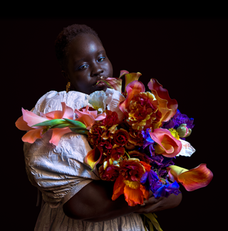 Foto einer Person mit wenig Licht, die einen bunten Blumenstrauß im Arm hält.